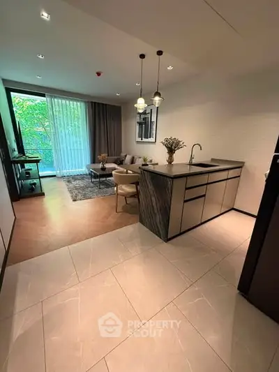 Modern open-layout living room with sleek kitchen and cozy seating area, featuring elegant lighting and large windows.