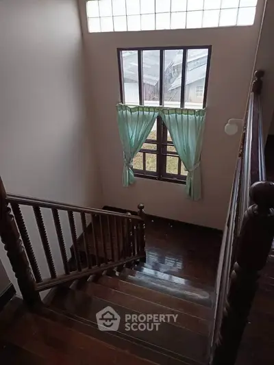 Charming staircase with wooden railing and large window with green curtains