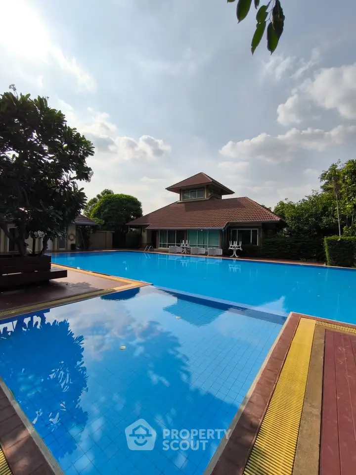 Stunning poolside view with modern house and lush greenery under a clear blue sky.