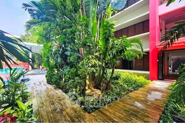 Lush tropical garden pathway in modern residential complex with vibrant red accents and pool view.