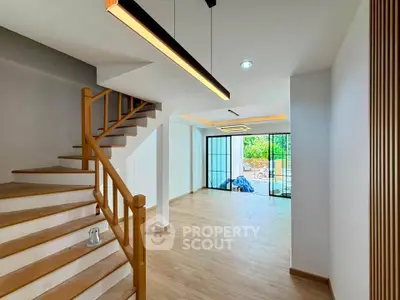 Spacious modern living area with wooden staircase and large windows offering natural light.