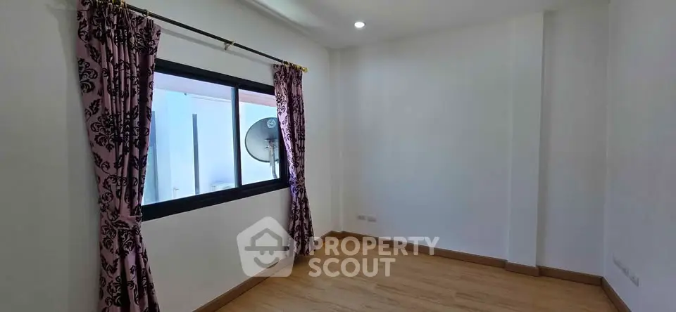 Spacious empty room with wooden flooring and large window, ideal for customization.