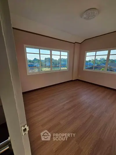 Spacious sunlit room with large windows and wooden flooring, perfect for a cozy living space.