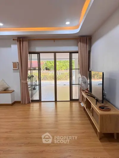 Spacious living room with wooden flooring and large glass doors leading to a balcony.