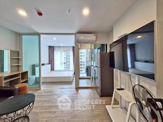 Modern living room with sleek design, large TV, and open layout leading to a bedroom with city views.