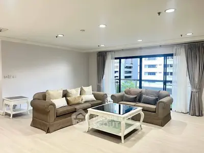 Spacious living room with elegant sofas and large windows offering city views.