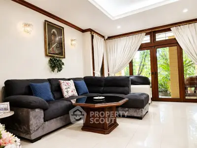 Elegant living room with plush sofa, stylish decor, and large windows offering lush garden views.