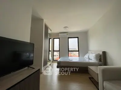 Modern bedroom with large windows and natural light, featuring a cozy bed and sleek TV setup.