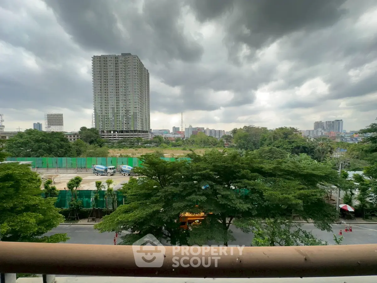 Stunning cityscape view from a balcony overlooking lush greenery and modern high-rise buildings.
