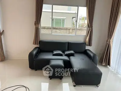 Modern living room with sleek black leather sofa and large windows offering natural light.