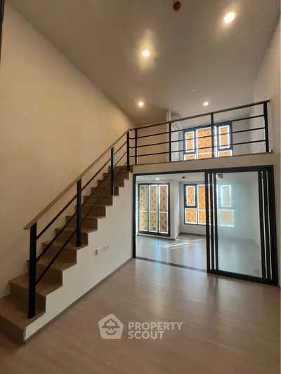 Spacious modern loft with high ceilings and large windows, featuring a stylish staircase and open layout.