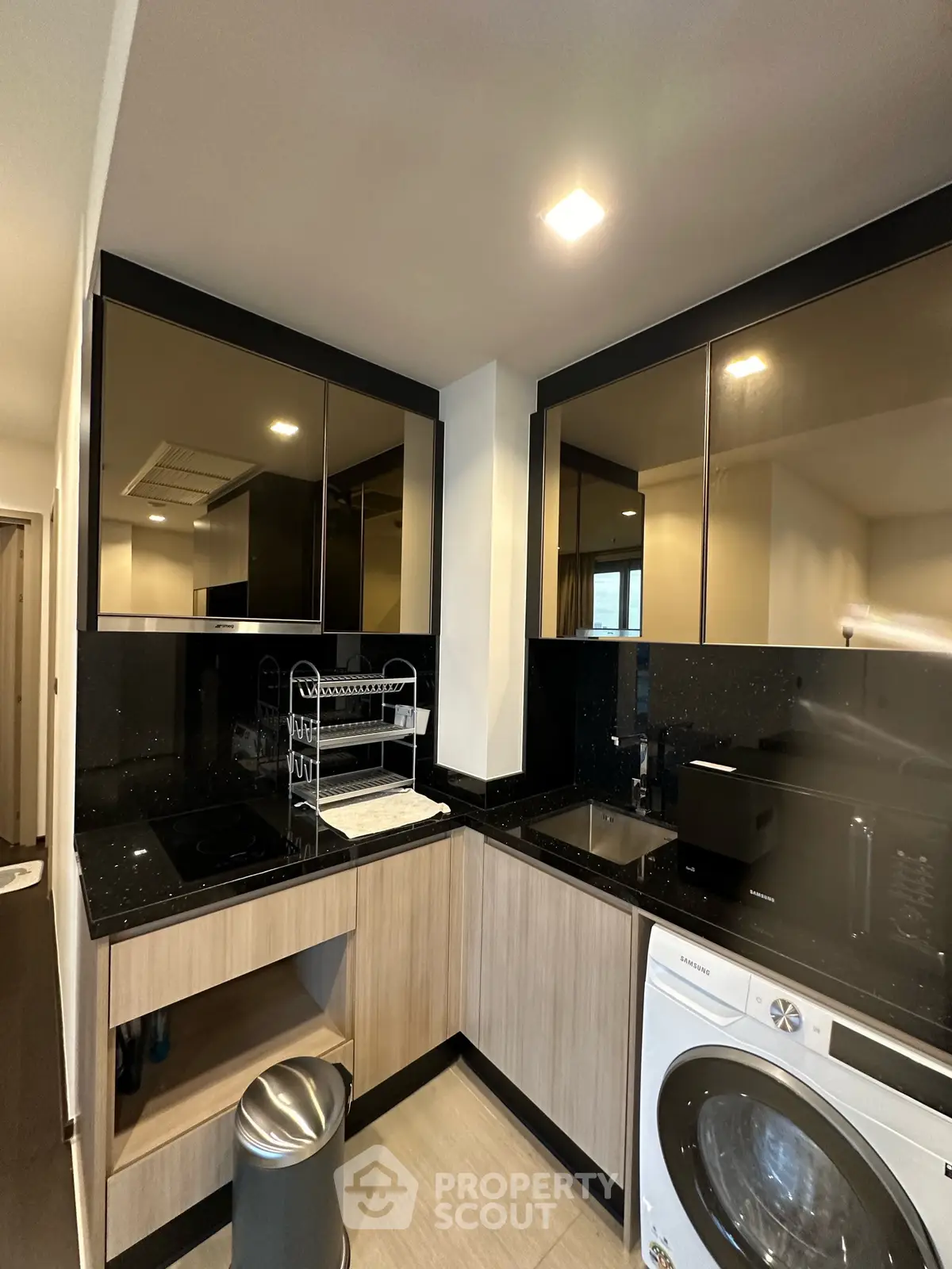 Modern kitchen with sleek black countertops and built-in appliances, featuring a washing machine and ample storage.