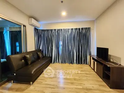 Modern living room with sleek black sofa, wooden flooring, and elegant blue curtains.