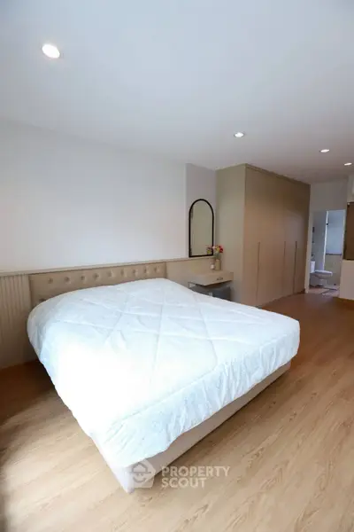 Spacious bedroom with modern design and ample natural light, featuring a cozy bed and sleek wooden flooring.