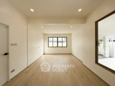 Spacious empty room with wooden flooring and large windows in a modern home.