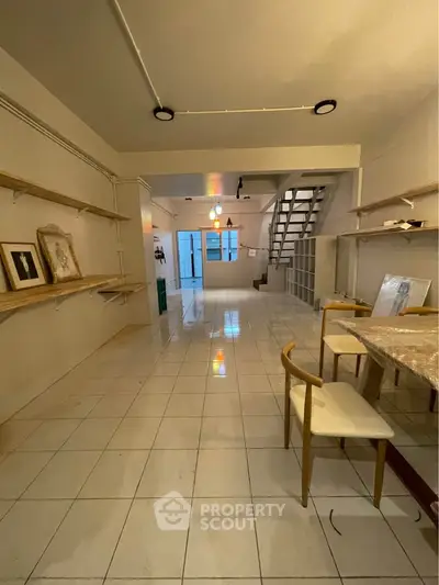 Spacious open-plan living area with modern decor and ample natural light, featuring stylish shelving and a sleek staircase.