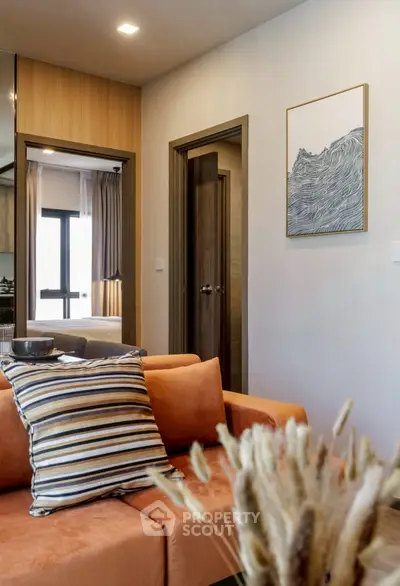 Modern living room with stylish decor and cozy orange sofa, featuring a glimpse into a bedroom.