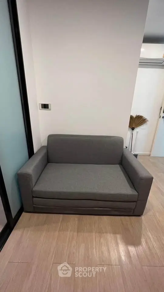 Modern compact gray sofa in a stylish minimalist room with wooden flooring.