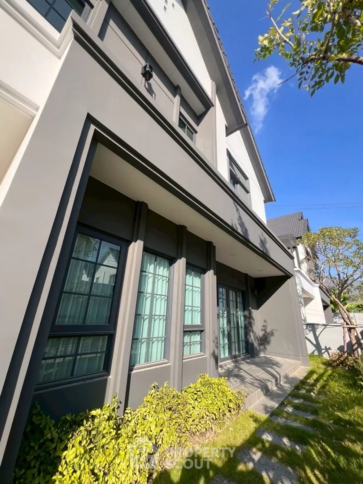 Modern two-story house exterior with lush greenery and clear blue sky