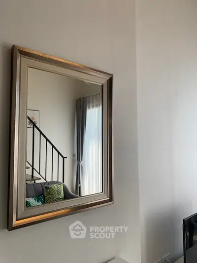 Modern living room with stylish mirror and staircase, featuring elegant decor and natural light.