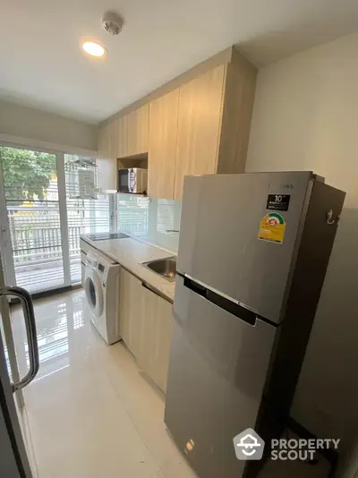 Modern kitchen with appliances including fridge and washing machine, featuring sleek cabinetry and balcony view.