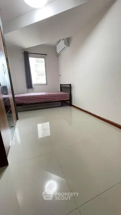 Spacious bedroom with polished floors and natural light, featuring a cozy bed and air conditioning.