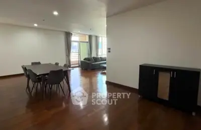 Spacious modern living room with dining area and balcony access, featuring sleek furniture and wooden flooring.