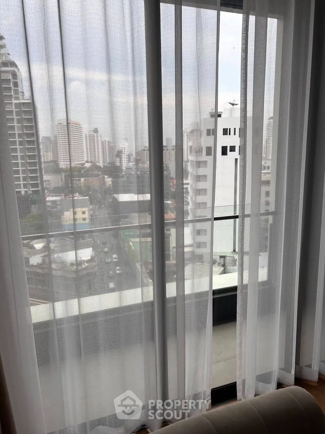 Stunning cityscape view from high-rise apartment window with sheer curtains.