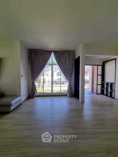 Spacious living room with large window and elegant curtains, showcasing modern interior design.