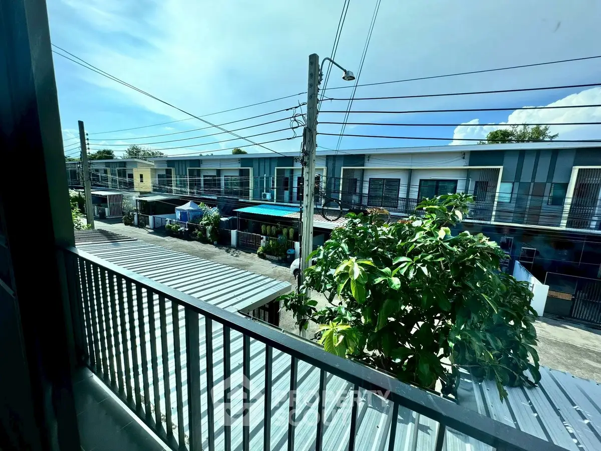 Charming residential street view from a balcony, showcasing modern townhouses and lush greenery.