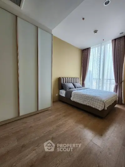 Spacious bedroom with large window and modern decor in a luxurious apartment.