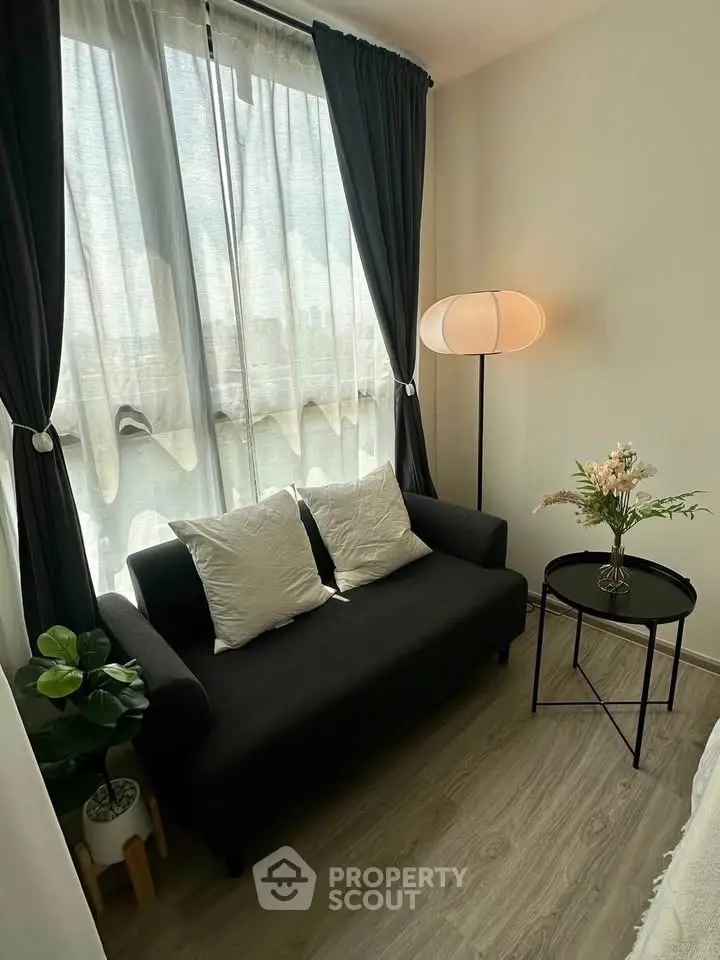 Cozy living room with elegant sofa, floor lamp, and natural light through large window.