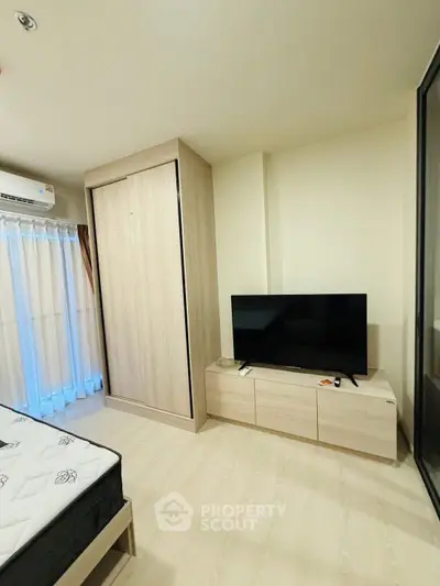 Modern bedroom with sleek wardrobe and flat-screen TV, featuring light wood flooring and natural light.