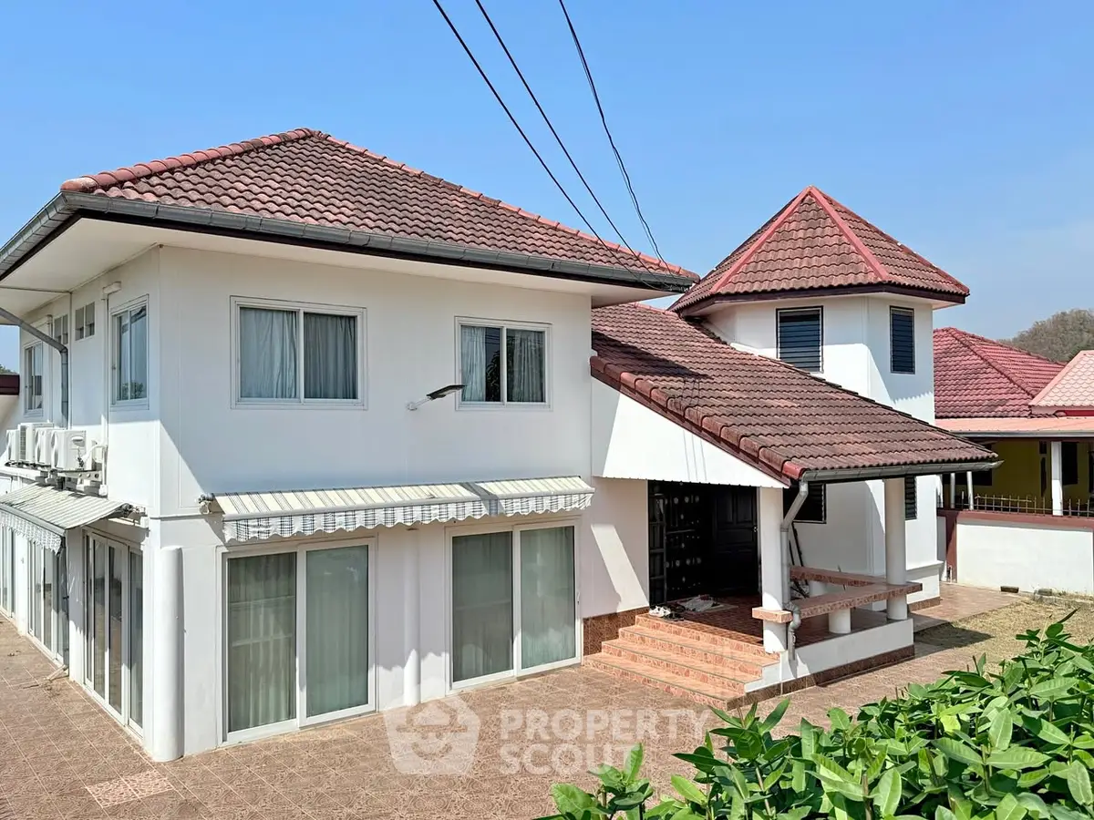 Charming two-story house with red-tiled roof and spacious patio in sunny neighborhood.
