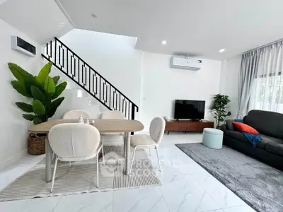 Modern living room with stylish dining area and staircase, featuring sleek furniture and bright decor.