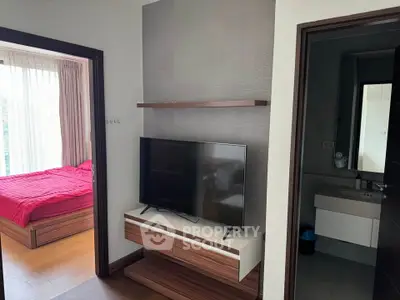 Modern apartment interior with bedroom and TV area, featuring sleek wooden furniture and natural light.