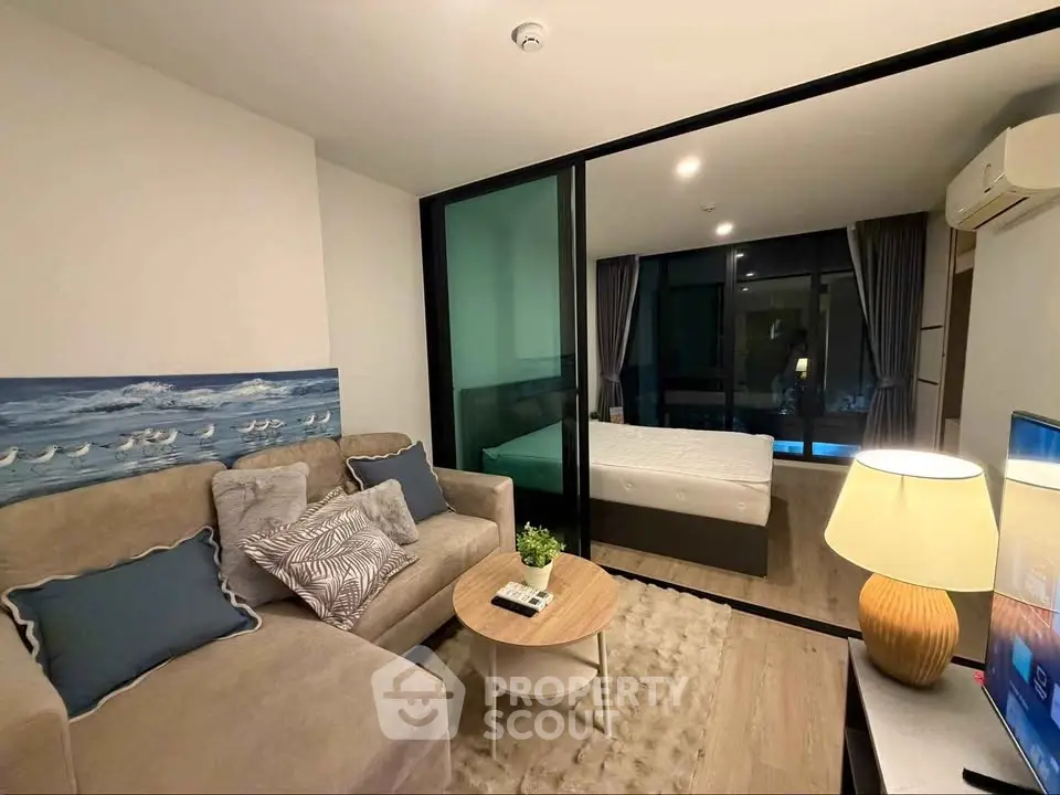 Modern living room with cozy sofa and adjacent bedroom separated by glass partition.