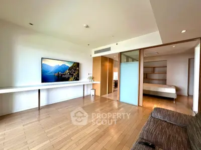 Spacious modern living room with wooden flooring and large TV, adjacent to a cozy bedroom.