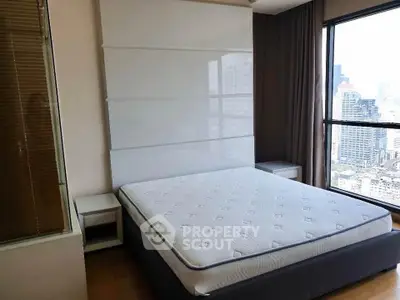 Modern bedroom with city view, featuring a large bed and floor-to-ceiling windows.