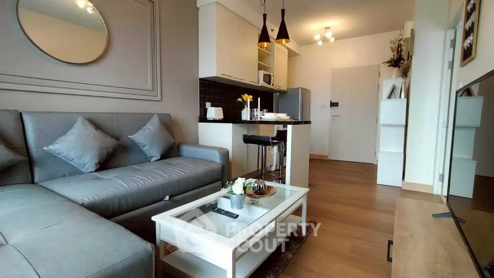 Modern living room with stylish decor and open kitchen layout, featuring a cozy gray sofa and elegant lighting.