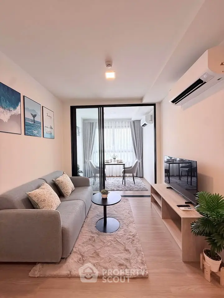 Modern living room with stylish decor and open view to dining area, featuring cozy sofa and sleek TV setup.