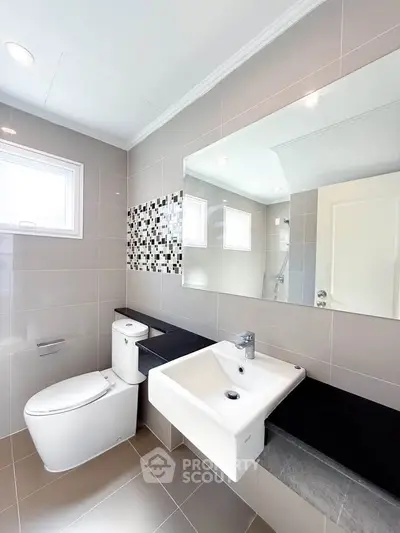 Modern bathroom with sleek fixtures and stylish tile accents, featuring a large mirror and natural light.