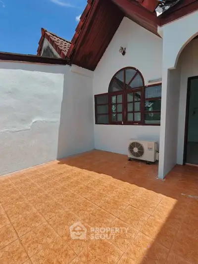 Charming outdoor patio with terracotta tiles and arched window, perfect for relaxation and entertaining.