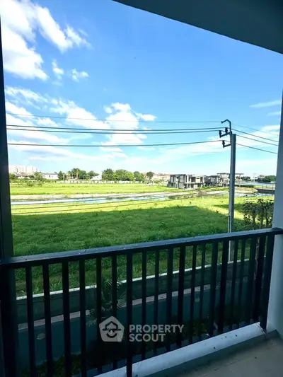 Scenic balcony view overlooking lush green fields and distant buildings under a clear blue sky.