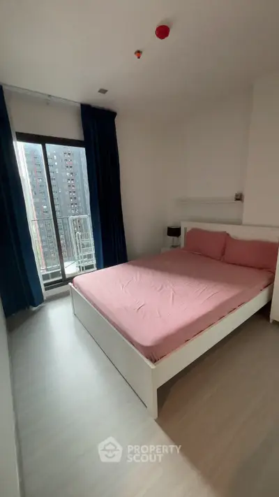 Spacious bedroom with large window and city view, featuring modern furnishings and pink bedding.