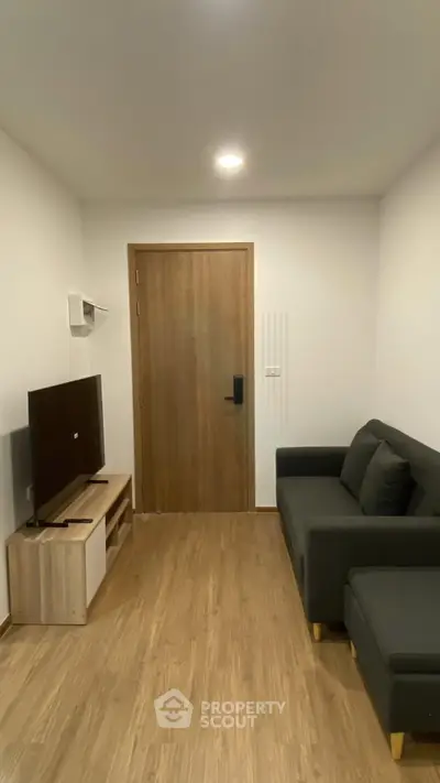 Cozy living room with modern sofa and flat-screen TV, featuring wooden flooring and minimalist decor.