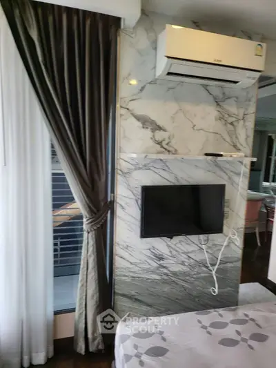 Modern bedroom with marble accent wall, air conditioning, and wall-mounted TV