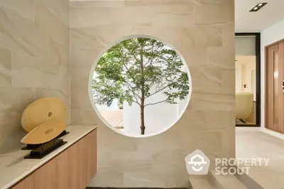 Elegant modern interior with circular window and tree view, showcasing minimalist design and natural light.