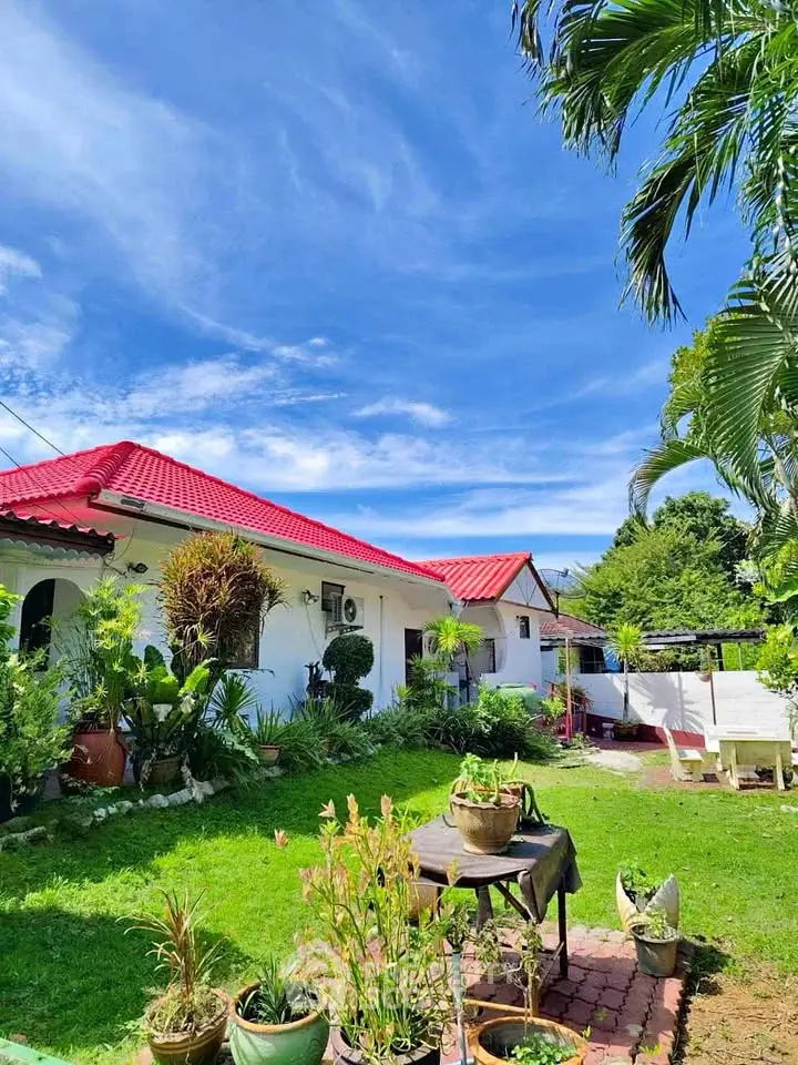 Charming white house with red roof and lush green garden under a clear blue sky.