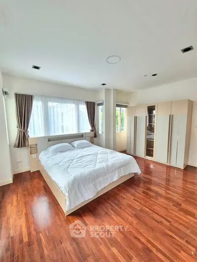 Spacious bedroom with wooden flooring and large windows for natural light
